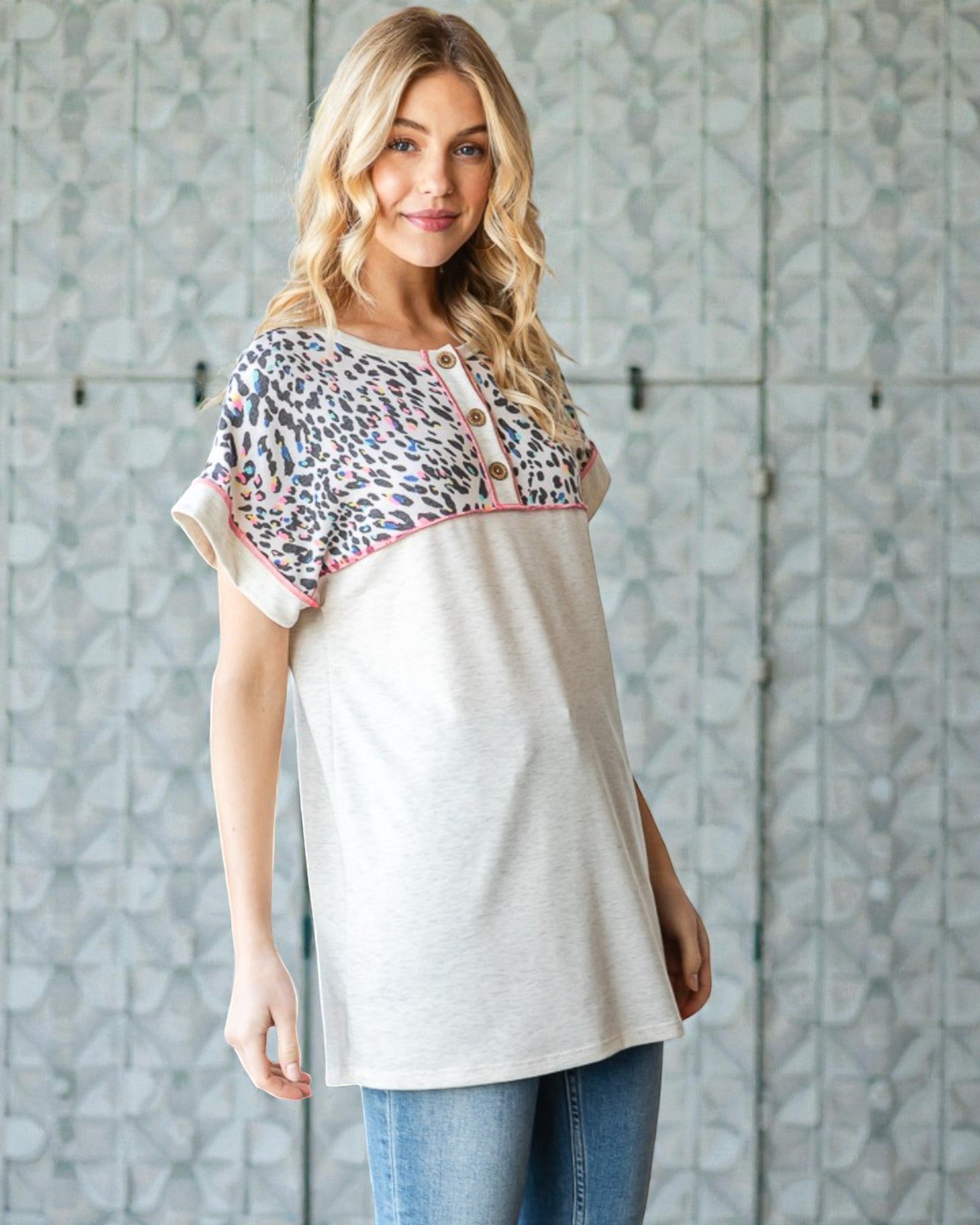 Woman wearing a white top with a patterned sleeve against a textured wall.