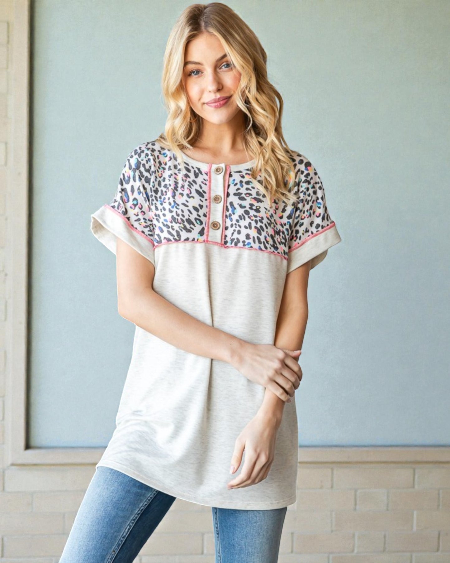 Woman wearing a white blouse with leopard print sleeves against a light blue wall.