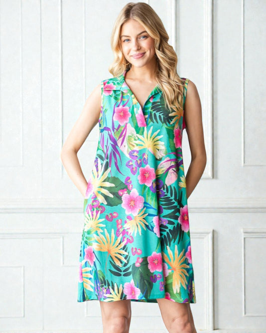 Woman wearing a colorful tropical print dress against a white paneled wall.