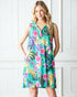 Woman wearing a colorful tropical print dress against a white paneled wall.