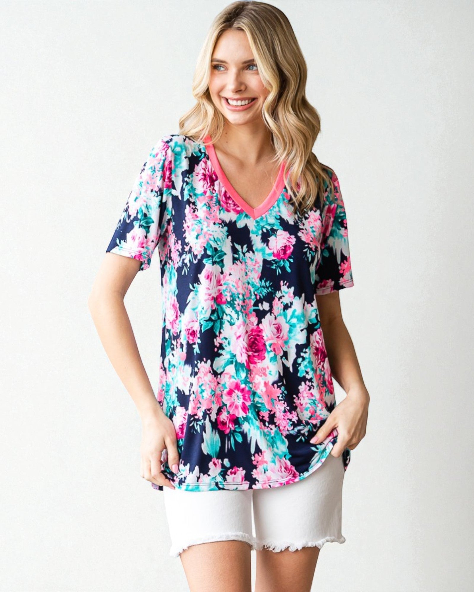 Woman wearing a colorful floral tunic with white shorts on a plain background