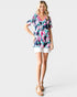 Woman wearing a floral dress and white shorts on a plain background