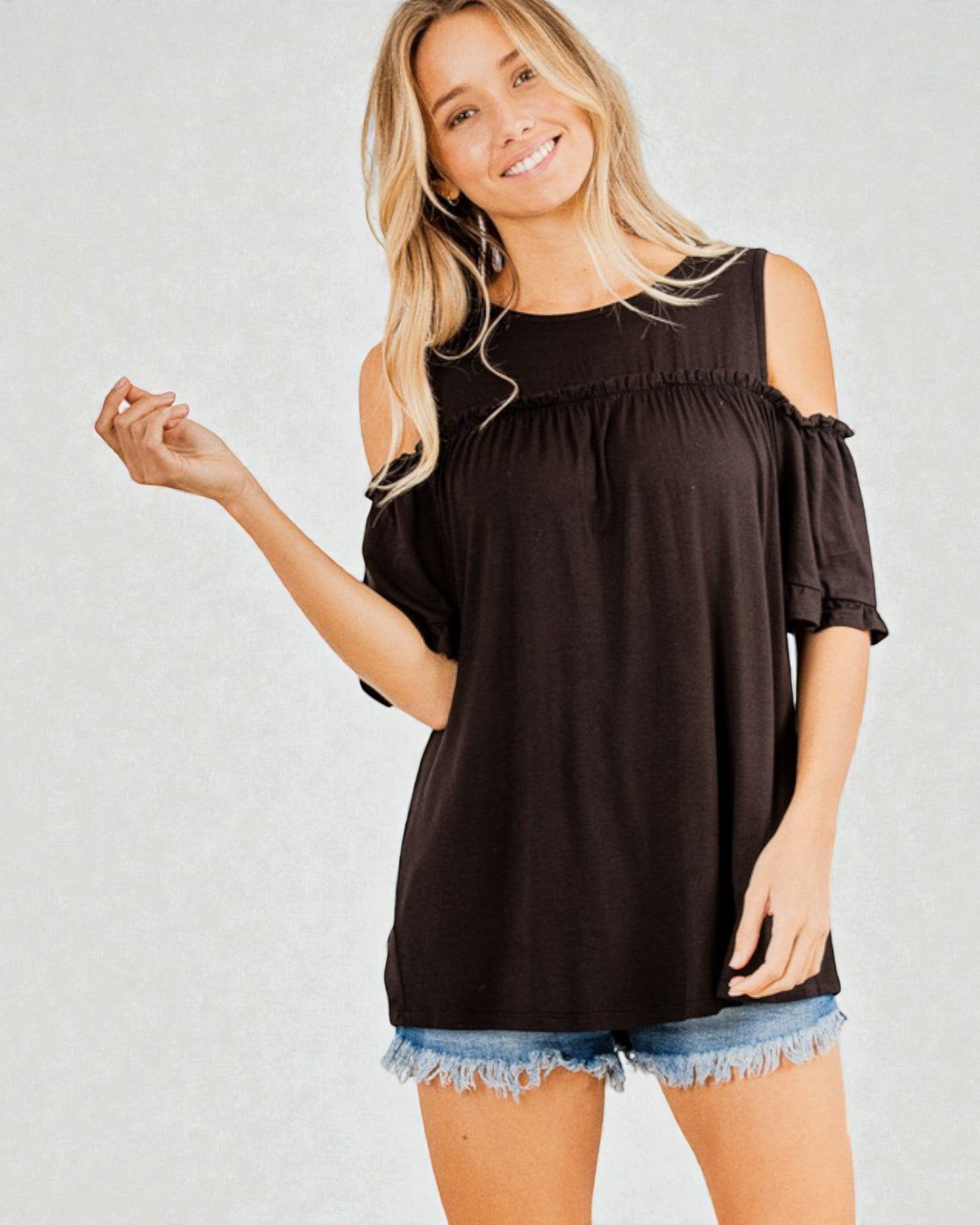 Woman wearing a black off-shoulder top and denim shorts on a plain background