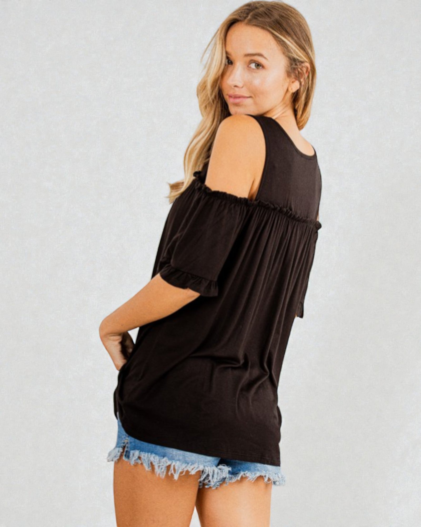Woman wearing a black off-shoulder top and denim shorts on a plain background