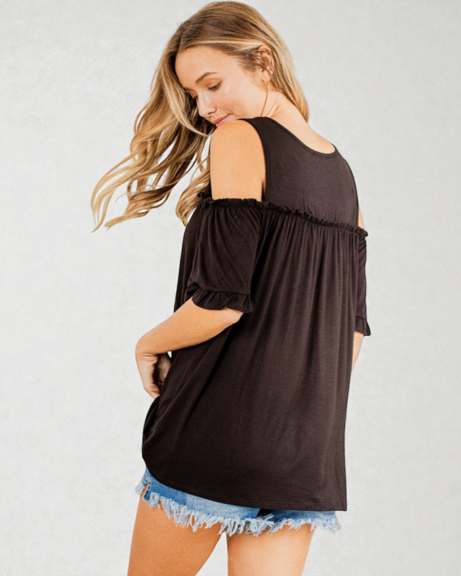 Woman wearing a black off-shoulder top with denim shorts on a plain background
