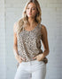 Woman wearing a leopard print tank top and white pants against a light brick wall.