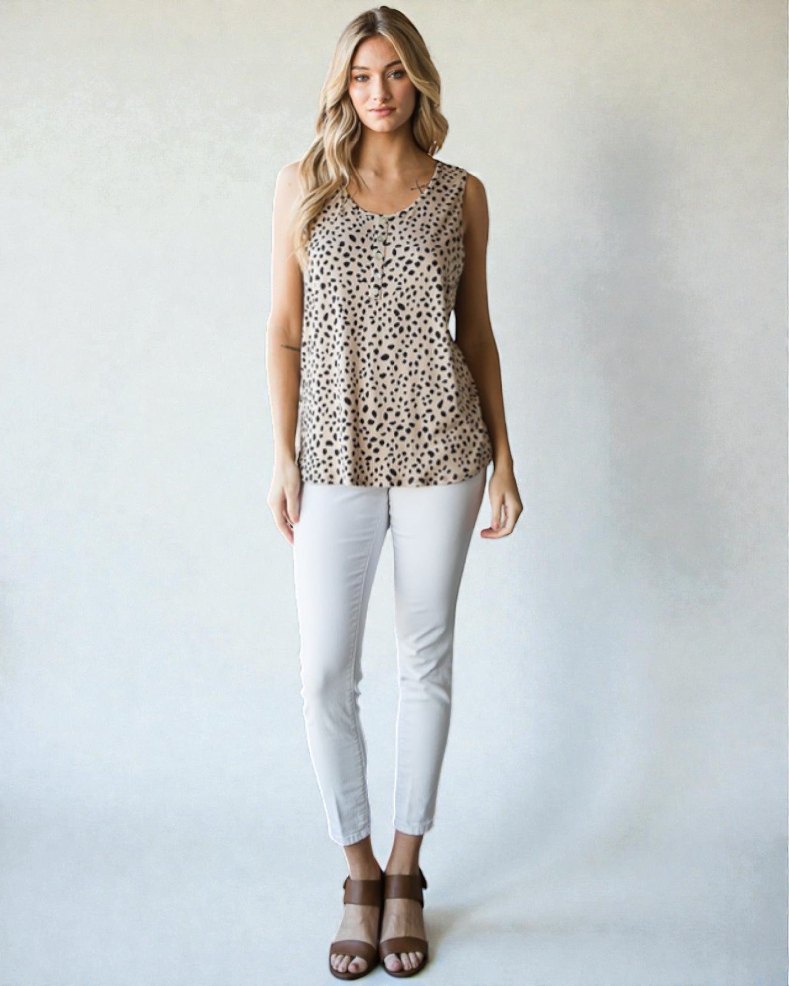 Woman wearing a leopard print sleeveless top and white pants against a plain background