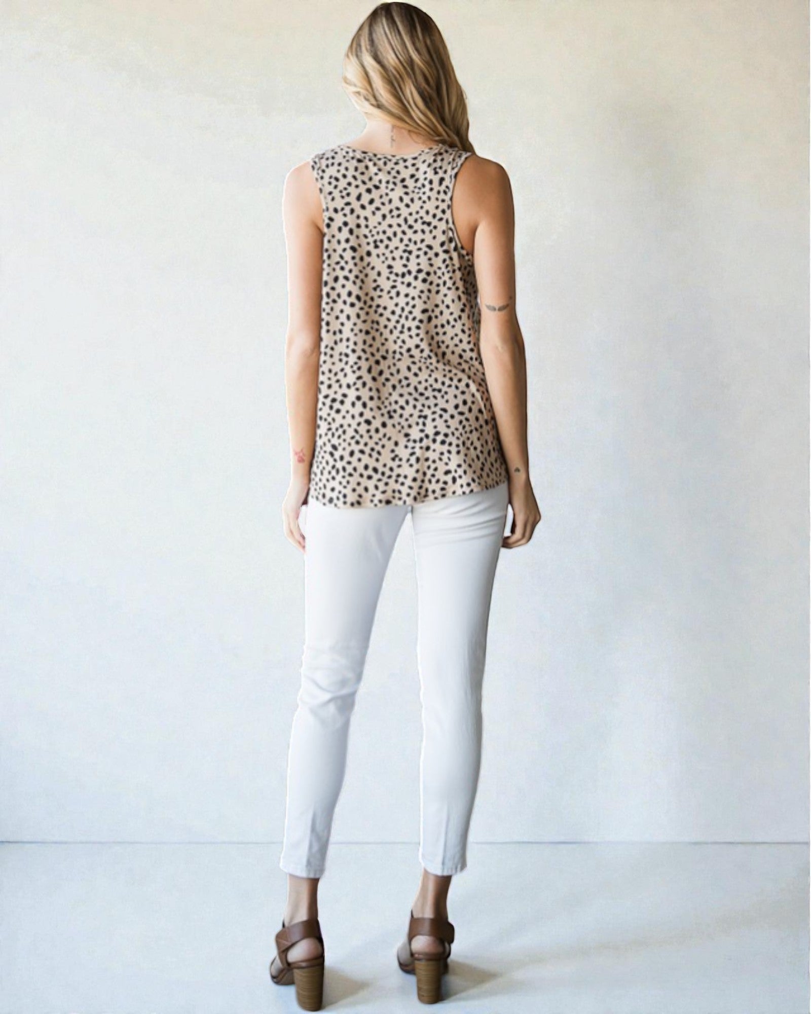 Woman wearing a leopard print sleeveless top and white pants on a plain background
