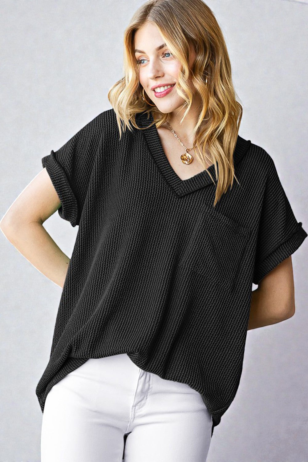 Woman wearing a black textured top and white pants against a gray background