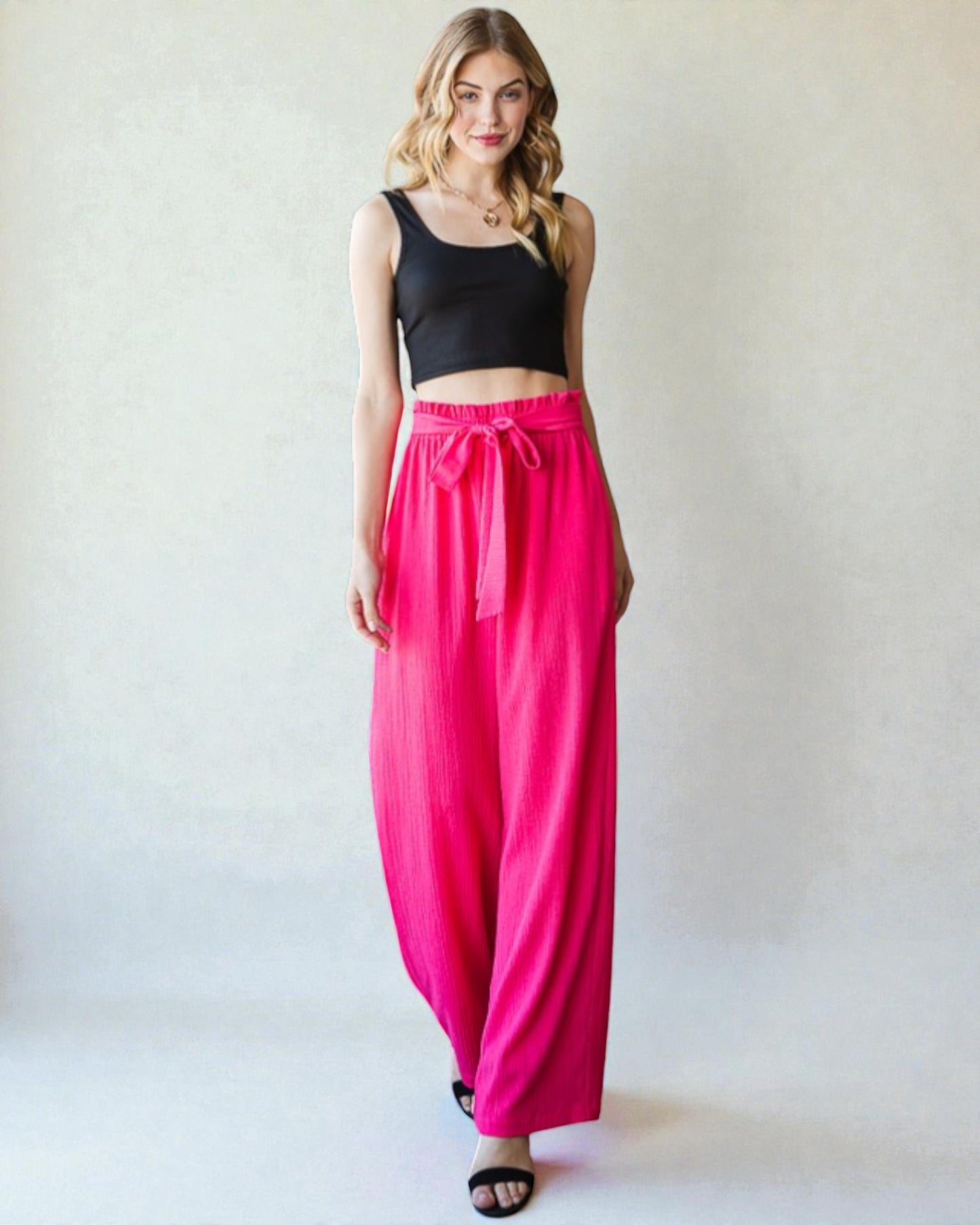 Woman wearing a black top and bright pink pants on a white background