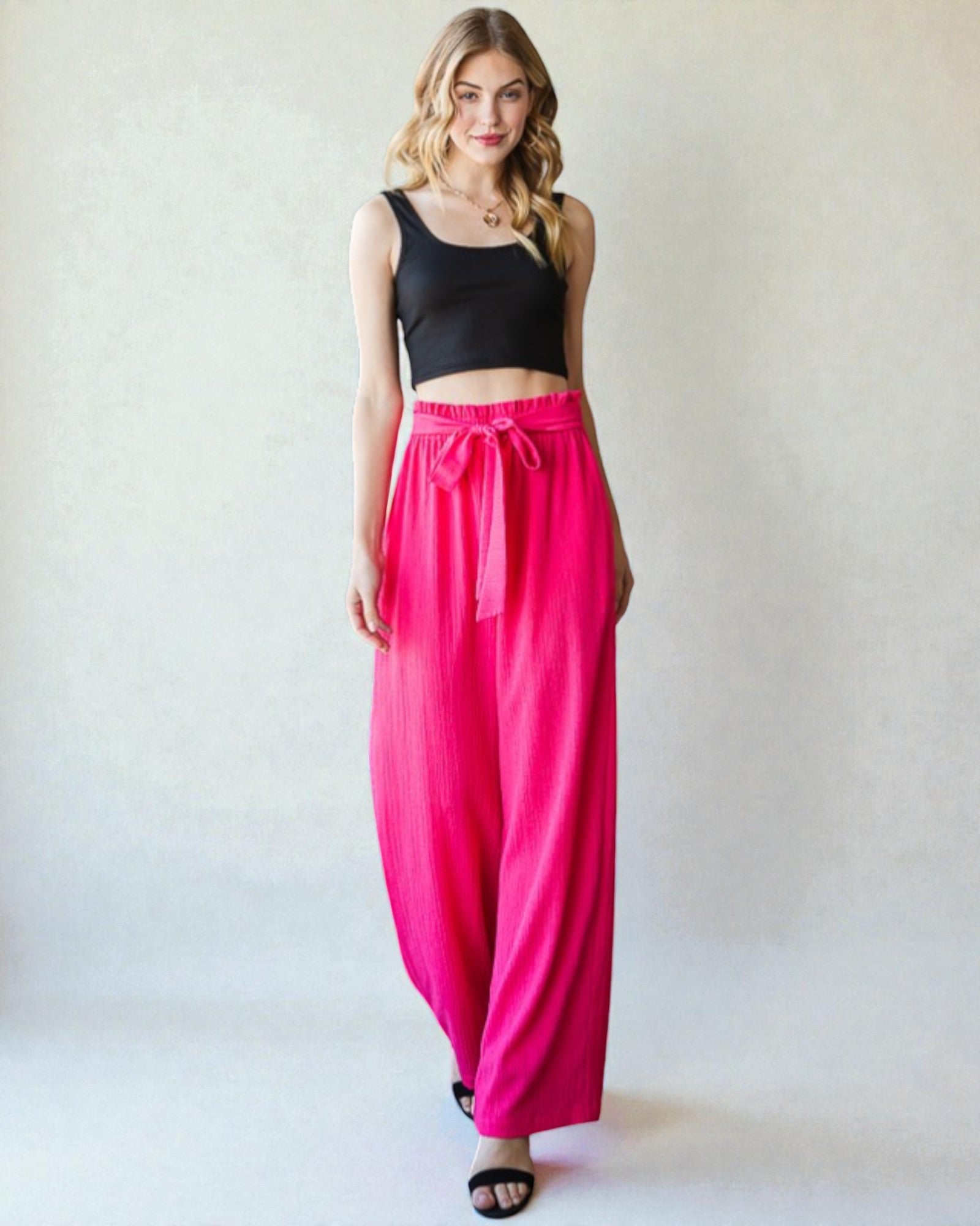 Woman wearing a black top and bright pink pants on a white background