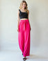 Woman wearing a black top and bright pink pants on a white background