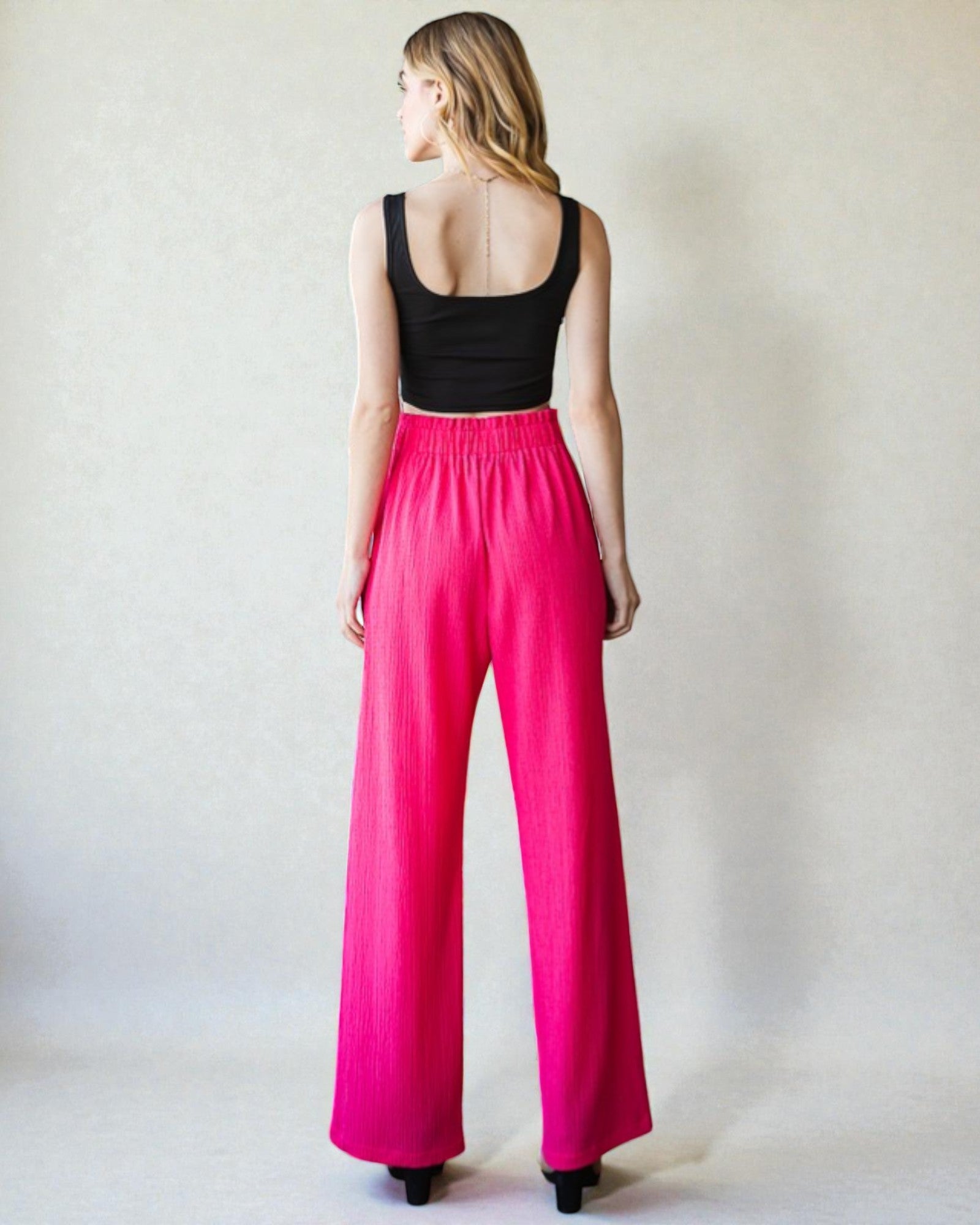 Person wearing a black top and bright pink pants against a plain background