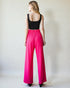 Person wearing a black top and bright pink pants against a plain background