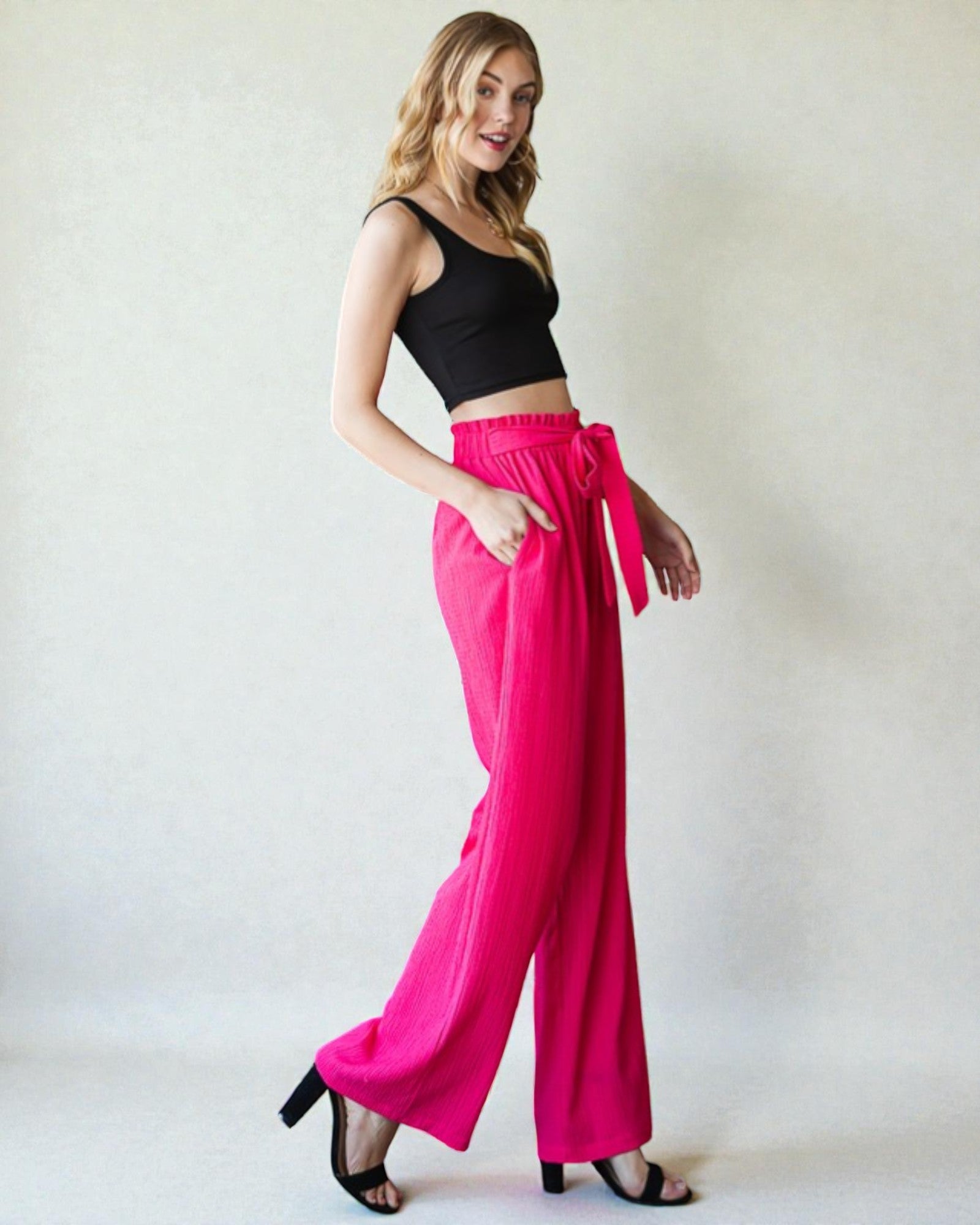 Woman wearing a black top and bright pink pants against a white background