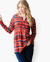 A woman modeling a long-sleeve button-front tunic top with a red, orange, and navy geometric pattern, paired with dark blue jeans, against a plain white background.