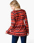 A woman shown from the back wearing a long-sleeve tunic top with a red, black, and blue geometric pattern, paired with dark blue jeans, against a plain white background.