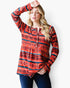 A woman modeling a long-sleeve bohemian-style tunic top with a red, orange, and black geometric pattern, paired with dark blue jeans against a plain white background.