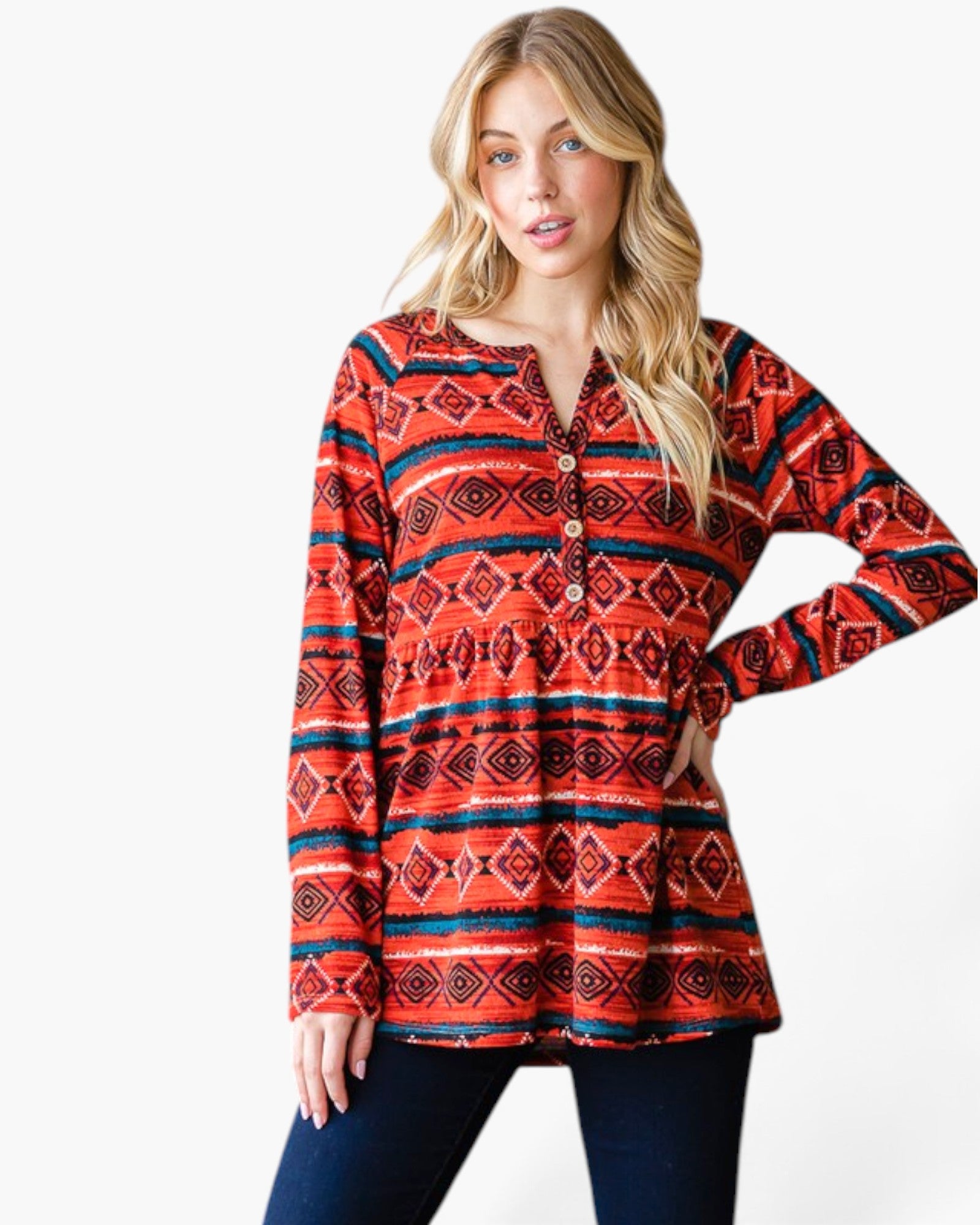 A woman modeling a long-sleeve tunic top with a red, orange, and navy geometric pattern, paired with dark blue jeans, against a plain white background.