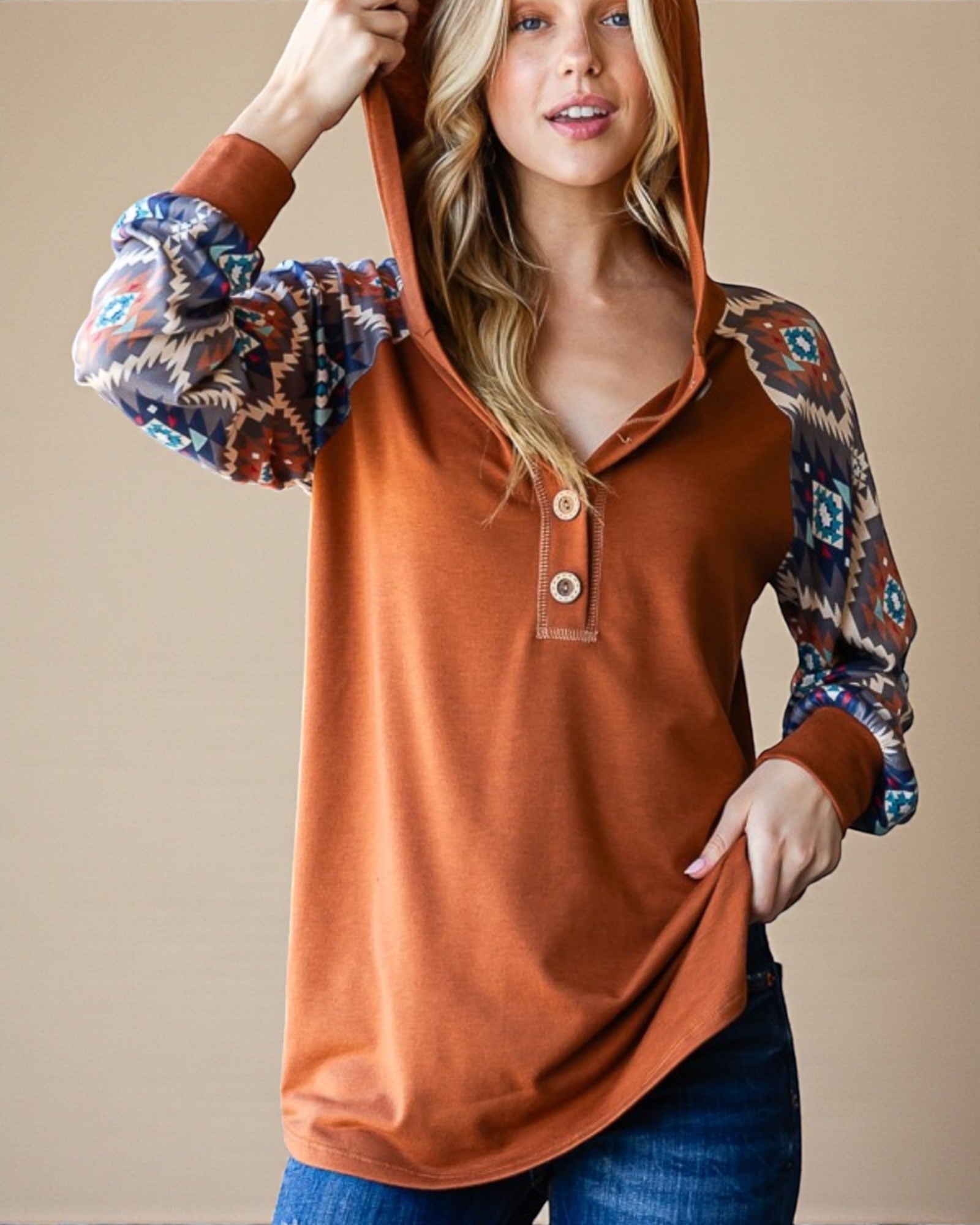 Woman wearing a rust-colored hoodie with patterned sleeves against a beige background
