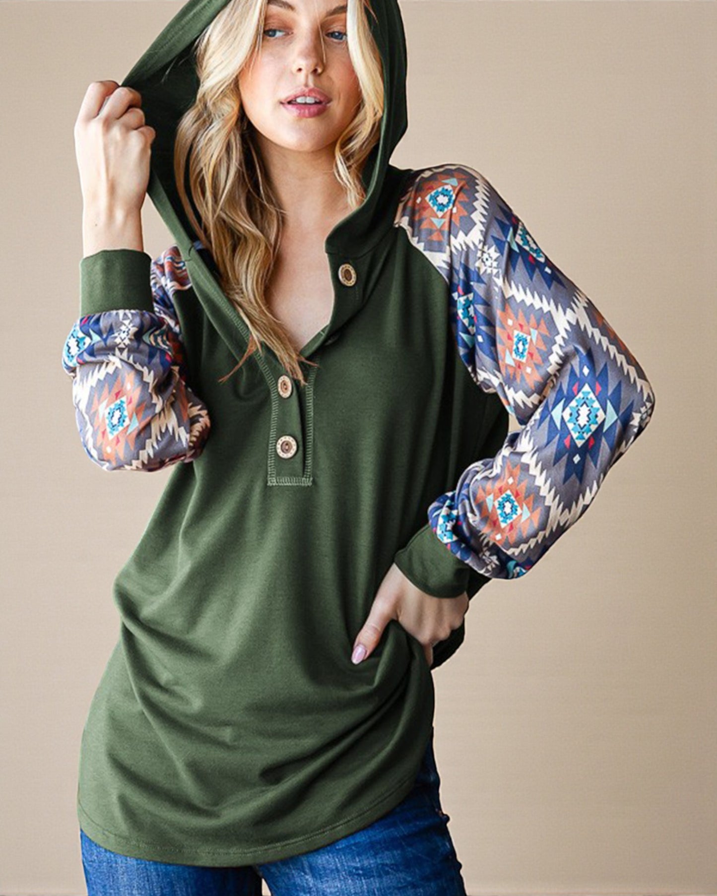 Woman wearing a green hoodie with patterned sleeves against a beige background