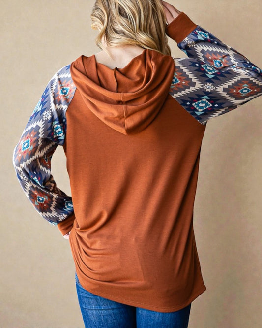 Person wearing a rust-colored hoodie with patterned sleeves against a beige background