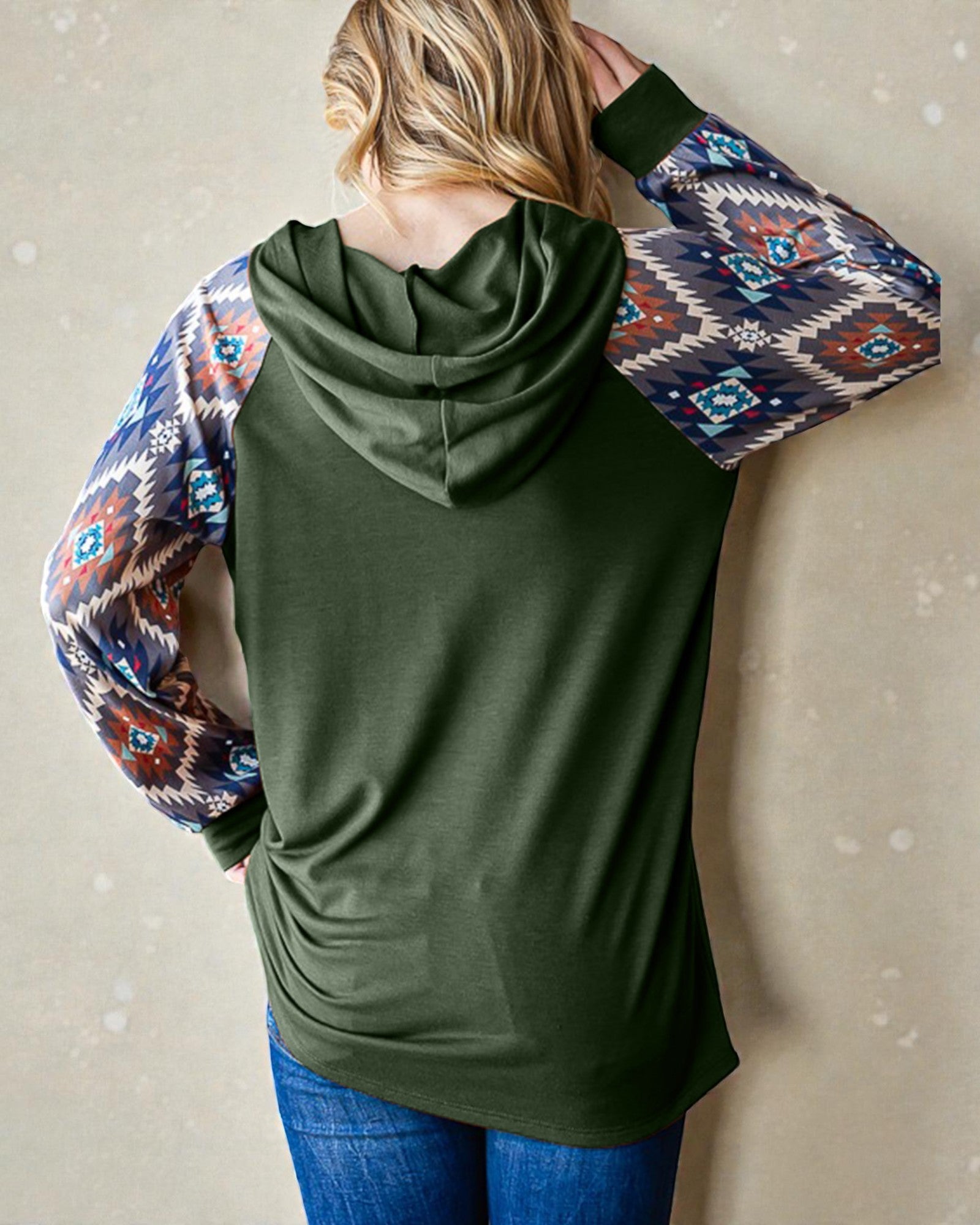 Green hoodie with patterned sleeves worn by a person against a beige wall.