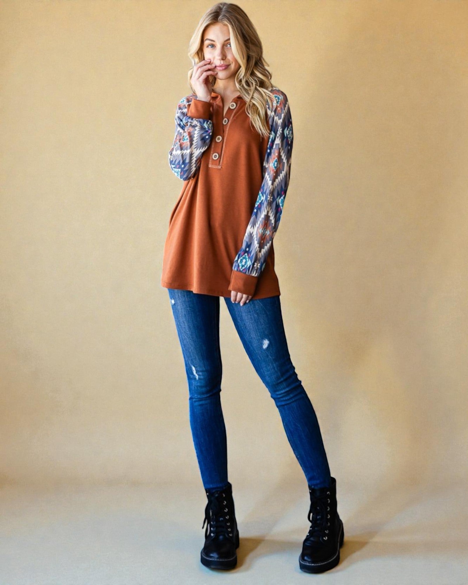 Woman wearing a brown top with plaid sleeves and blue jeans against a beige background