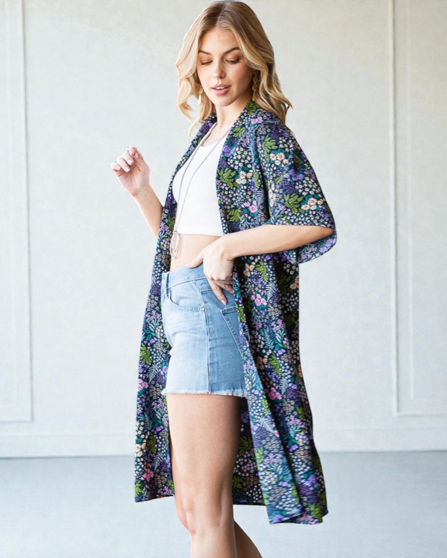 Woman wearing a floral kimono over a white top and denim shorts against a white background