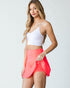 Woman wearing a white crop top and coral skirt on a plain background