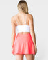 Woman wearing a white top and coral skirt on a plain background