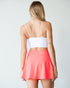 Woman wearing a white crop top and coral skirt on a plain background