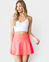 Woman wearing a white crop top and coral skirt on a plain background