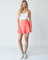 Woman wearing a white crop top and coral skirt on a plain background