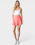 Woman wearing a white tank top and coral skirt on a white background
