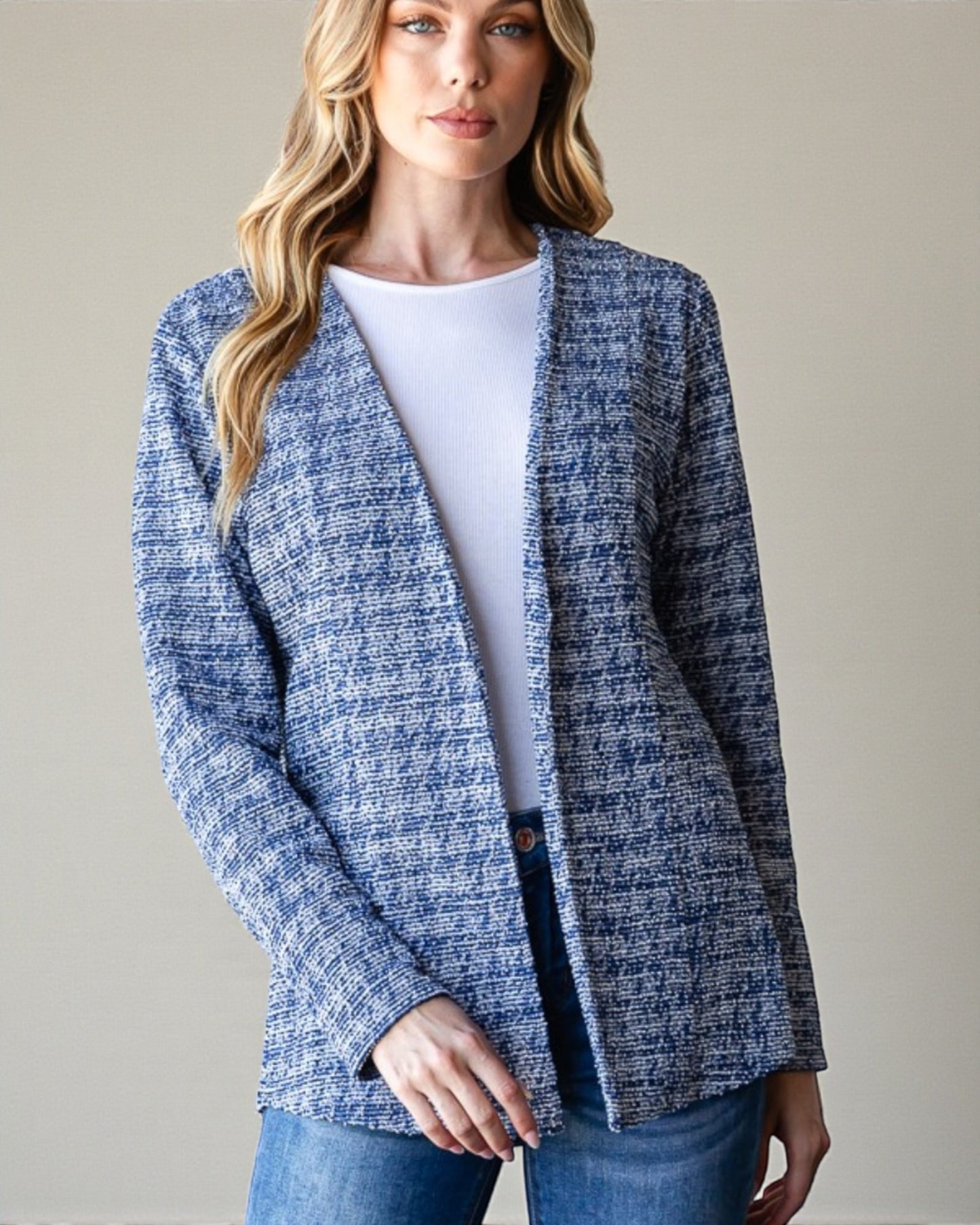 Woman wearing a blue textured cardigan over a white shirt and jeans on a plain background