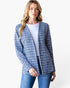 A woman modeling a blue and white textured tweed open-front cardigan over a white top and blue jeans, photographed against a clean white studio background.