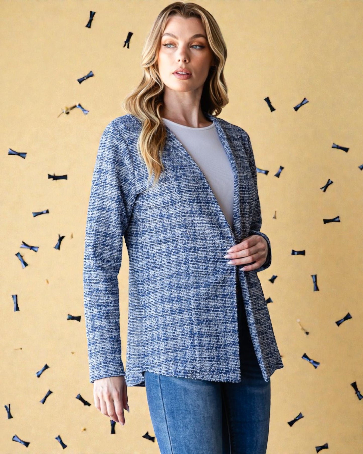 Woman wearing a blue textured blazer over a white shirt with a beige background featuring decorative elements.