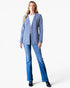 A woman modeling a blue and white patterned tweed blazer over a white top and blue jeans, standing against a plain white studio background.
