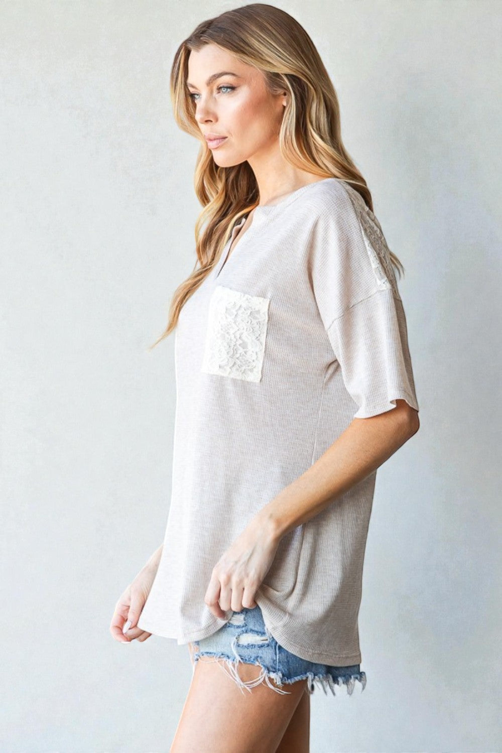 Woman wearing a beige oversized shirt with a pocket on a plain background