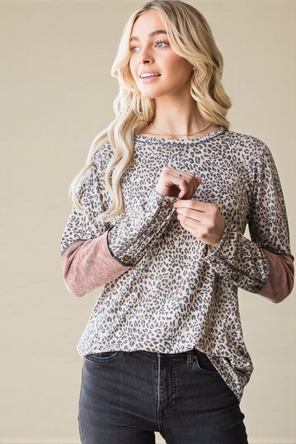 Woman wearing a leopard print top with pink cuffs against a beige background