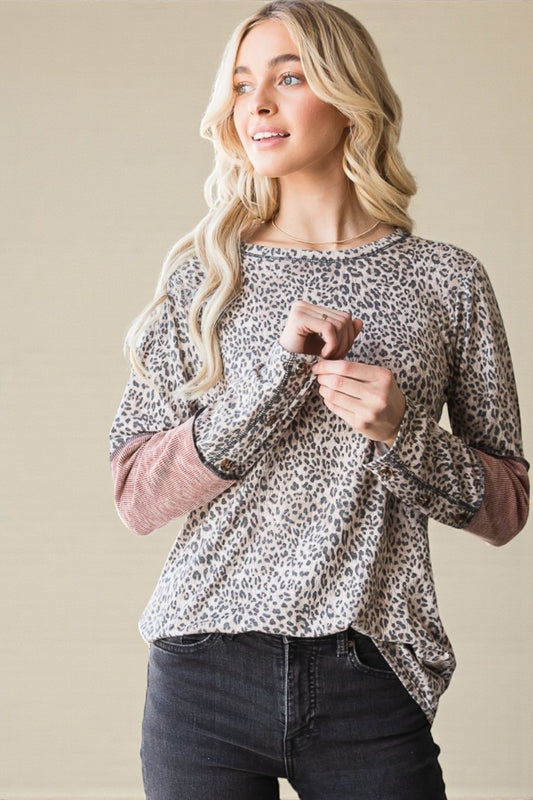 Woman wearing a leopard print top with pink cuffs against a beige background