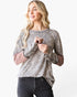 A woman modeling a long-sleeve top with a beige and brown leopard print pattern and contrasting dusty rose sleeves, paired with black jeans against a plain white background.