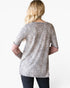 A woman viewed from the back wearing a leopard-print tunic top with dusty rose three-quarter sleeves and dark jeans, against a plain white background.