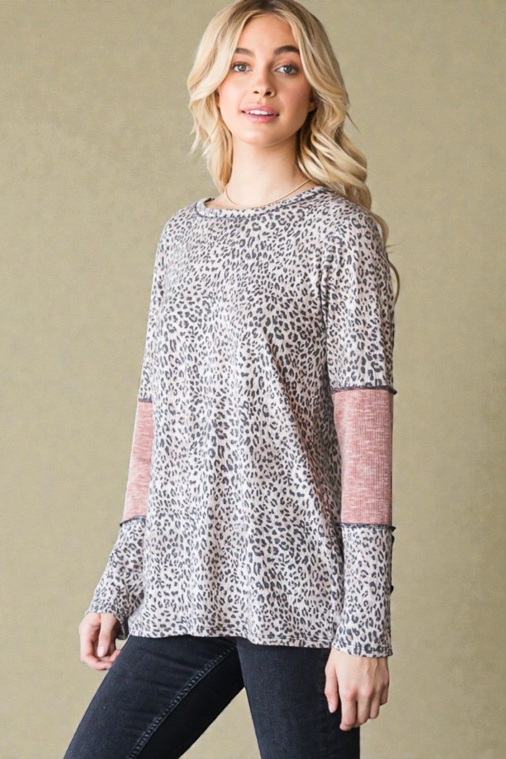 Woman wearing a leopard print top with pink sleeves against a beige background