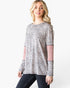 A woman modeling a long-sleeve top with a gray, black, and white leopard print pattern and contrasting dusty pink knit sleeve panels, paired with dark jeans against a plain white background.