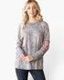 A woman modeling a long-sleeve top with a beige and brown leopard print pattern and dusty rose mesh elbow patches, paired with dark jeans against a plain white background.