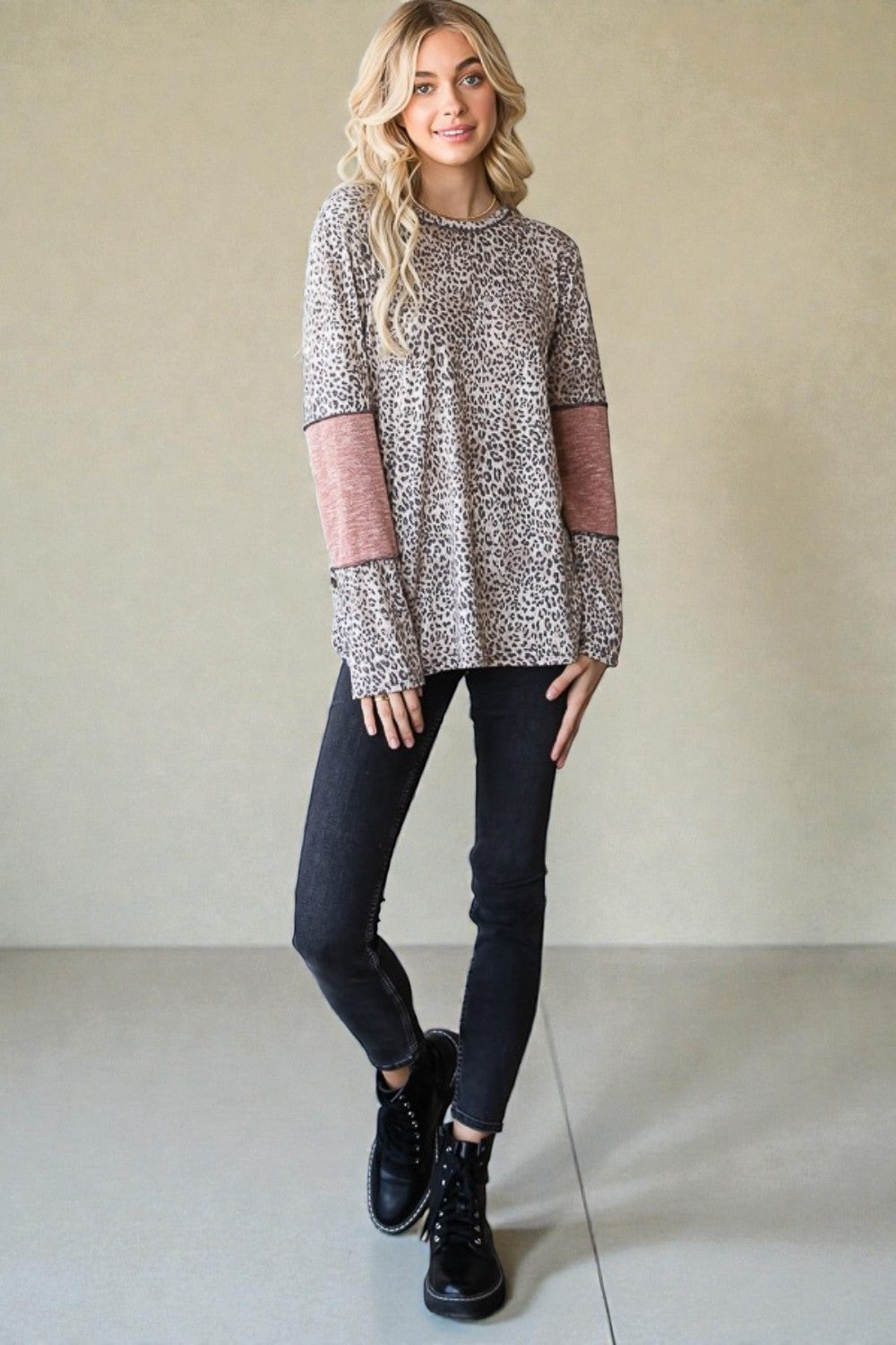 Woman wearing a patterned sweater with pink sleeves, black pants, and black boots against a plain background