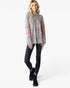 A woman modeling a long-sleeve knit top with a beige and black leopard print, dusty pink elbow patches, and flared cuffs, paired with black jeans and black lace-up boots against a white studio background.