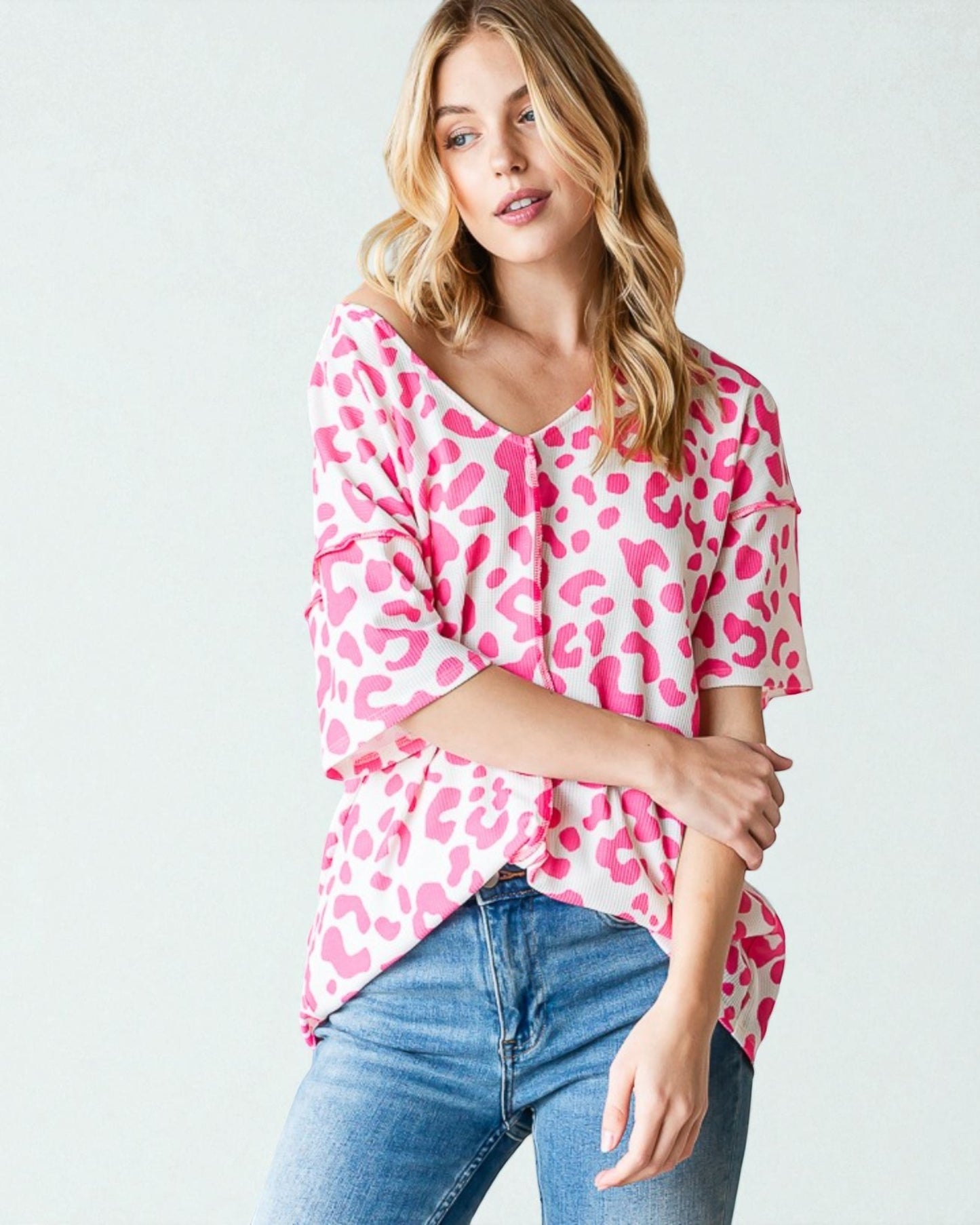 Woman wearing a pink leopard print top and blue jeans on a white background